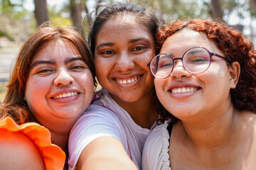 Three latin women are hugging and smiling in a park