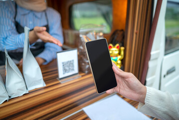Female barista showing qr code to woman to scan with cellphone for payment. Mockup or copy space. Small business of coffee shop or cafe on truck