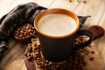 Flat white coffee in a black cup with coffee beans on rustic wooden table, french press on background.