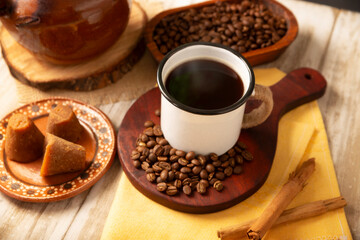 Cafe de Olla. Traditional Mexican coffee and basic ingredients for its preparation, coffee, cinnamon and piloncillo, served in a metallic cup called "peltre" on a rustic wooden surface.