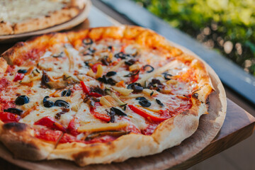 Pizza with cheese, vegetables and olives on a wooden stand. Delicious Italian cuisine. Vegetarian pizza close-up.