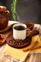 Cafe de Olla. Traditional Mexican coffee and basic ingredients for its preparation, coffee, cinnamon and piloncillo, served in a metallic cup called "peltre" on a rustic wooden surface.