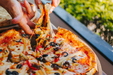 Men's hands tear off a slice of pizza with vegetable toppings, olives and stretching hot stretchy cheese. Process of eating pizza close-up. Delicious Italian pizza for friends and delivery