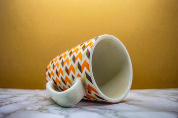 A stylish white ceramic mug with a vibrant retro zig zag pattern in brown, orange, and green lies...