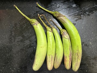 Green Slim Brinjals on Black Granite – Indian Long Eggplants Displayed Side by Side