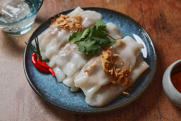 Plate of freshly prepared Bun-kuan paper rolls (bánh cuốn or similar). The rolls are neatly arranged on a dark blue ceramic plate, with a shiny, smooth surface indicating they are moist and tender. 
