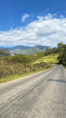 Image depicts a scenic rural landscape featuring a paved road that stretches into the distance, flanked by lush, green vegetation on both sides
