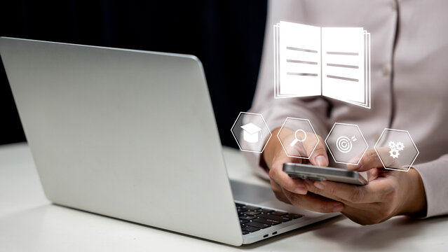 Businesswoman using a cellphone and showing a book icon. Laptop on the table. Technology innovation on a virtual screen. Concept of E-library