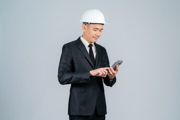 Smiling young Asian engineer or architect pointing at smartphone on grey background