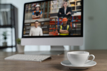 Online video conference and Coffee cupcomputer monitor displays video call with four diverse people different settings, placed wooden desk with