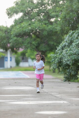 A young girl runs on a sidewalk in a park.