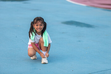 A young girl is kneeling on the ground with a green towel draped over her shoulder.