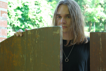 Young man peering through a wooden gate in a lush garden setting