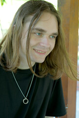 Smiling young man with long hair in a sunlit outdoor setting