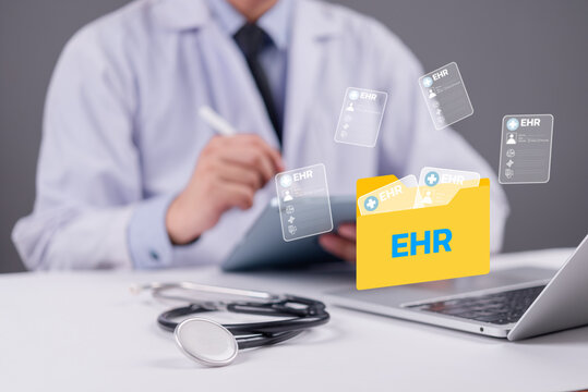 Doctor using digital tablet with EHR folder icon and medical records floating above laptop, representing electronic health records and modern healthcare technology concept.