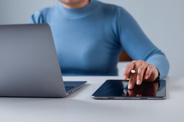 Close-up of businesswoman sitting at desk using stylus pen and digital tablet, working on laptop...