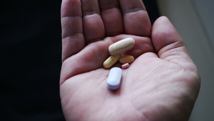 A close-up of an open hand holding a variety of pills, representing healthcare, medication, and...
