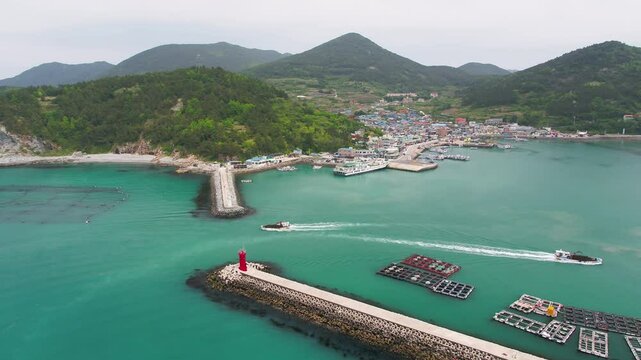 한국 해안의 어촌 마을을 항공 촬영한 장면. 붉은 등대, 양식장, 푸른 바다를 가르는 배들이 농어촌의 해양 삶을 보여준다.