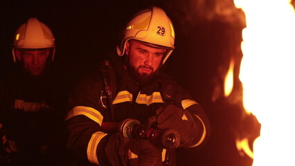 Brave firefighters battling intense flames at night. Firelight illuminates their determined faces as they work courageously in darkness. Dramatic scene of rescue, danger, and heroism.