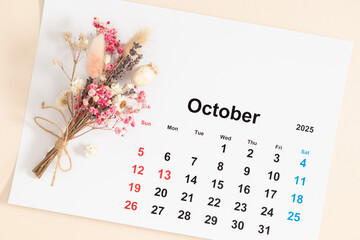 Close-up of paper sheet of calendar for october 2025 with beautiful small bouquet of dried flowers...