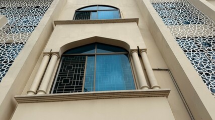 Fototapeta premium Beige Building with Arched Windows, Pillars, and Geometric Screen Details Low Angle View