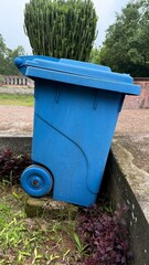 Blue Wheeled Trash Can with Lid in Garden Setting Near Succulent Plants