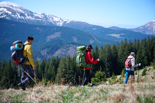 Experienced hikers walking on a mountain trail. Group of friends equipped with hiking gear climbing the mountain. Scenery of snowy mountains.