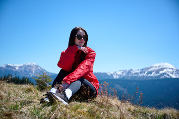 Hiker girl on background of snowy mountains. Young female in red sport jacket and sunglasses hiking...