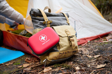 Red first aid kit on a backpack near a camping tent. Injuries and damage in the forest. Concept of...