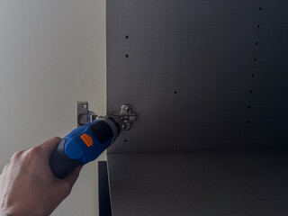 Installing cabinet hinge with electric screwdriver. DIY furniture assembly process, repair and construction tool action, fixing cabinet door, hardware installation, home improvement task, hands-on bui