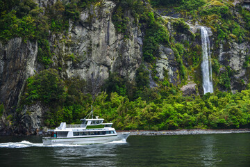 Boat near spectacular waterfall, Milford Sound fiord, New Zealand