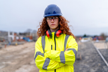 Construction site showcases confident female builder worker in bright safety gear during daytime activities at a bustling building project in the background