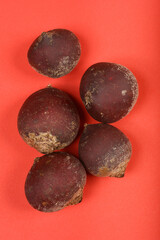 This top-down shot showcases five whole, unpeeled beetroots with their earthy textures, arranged on a vibrant red background