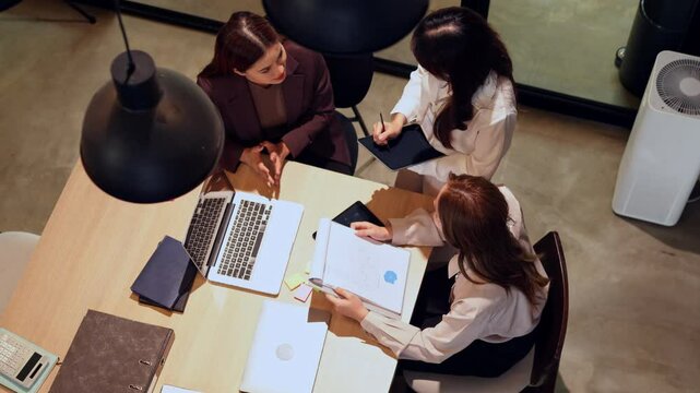 Team of Asian women working on laptops in industrial-style home office with collaborative and focused energy