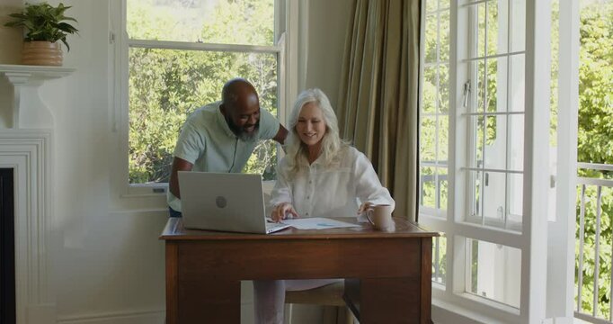 Senior couple sitting in home office viewing smartphone message, tossing papers, signing contract