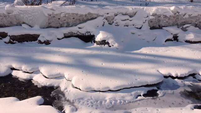 Slow-Moving Creek Flowing During Cold Winter Surrounded by Snow