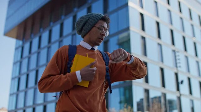 Worried young man checking time on smartwatch in city street