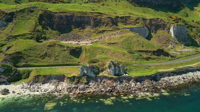 Wide, reversing aerial video of Madman's Window on the Causeway Coastal Route in County Antrim, Northern Ireland, UK, on a bright and sunny day. Filmed in 4K, 60FPS and with Rec709 color.