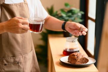 Close up of man in an apron holding a glass cup of black coffee and a piece of bread