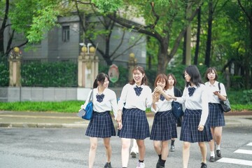 Obraz premium On a bright early summer morning in Pudong, Shanghai, seven Japanese high school girls wearing crisp summer uniforms are chatting as they cross a busy city street crosswalk on their way to school.