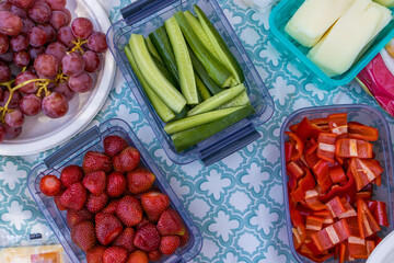 Clean and processed picnic vegetables in containers, sliced cucumbers, strawberries, bell peppers, cheese and grapes