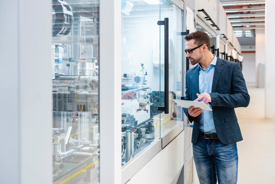 Young male employee inspecting machines in a production hall with a tablet