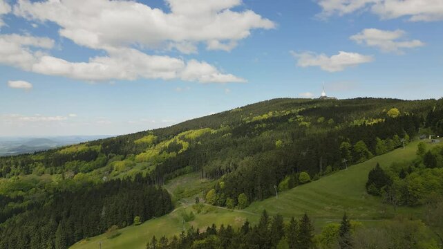 Aerial footage of forests and meadows around Jested mountain with its iconic tower, as paragliders and hang gliders soar nearby.