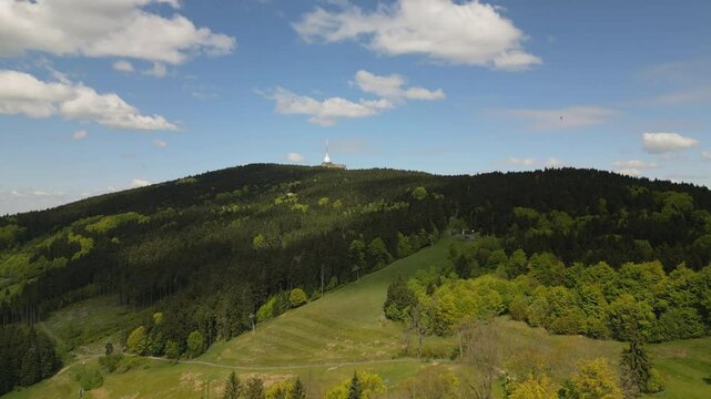 Aerial footage of forests and meadows around Jested mountain with its iconic tower, as paragliders and hang gliders soar nearby.