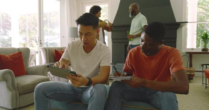 Prompted by tablet tap, diverse male friends tapping screen, writing notes, high-fiving on sofa