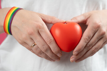 Woman with engagement ring and rainbow bracelet holding heart. 