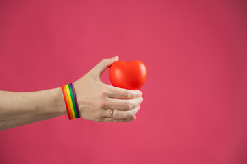 Woman with engagement ring and rainbow bracelet holding heart on pink background. Copy space. 