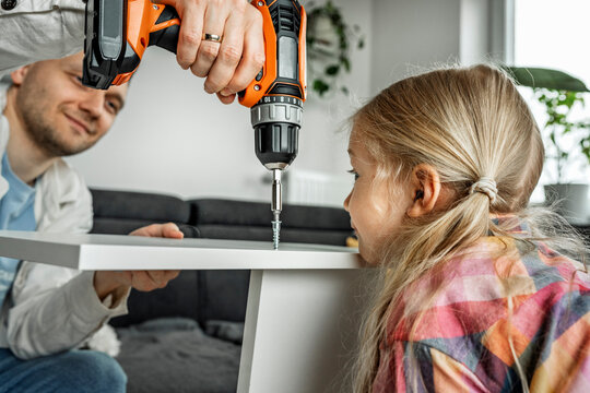 Father and daughter assembling furniture at home using a drill