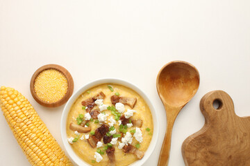traditional Ukriaina food Corn hominy porridge in a clay pot. Corn flour in a clay bowl and cob of ripe corn. Light background. Close-up. View from above.
