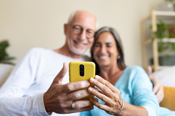 Mature couple relaxing sitting on the couch looking at mobile phone together. Selective focus on phone.